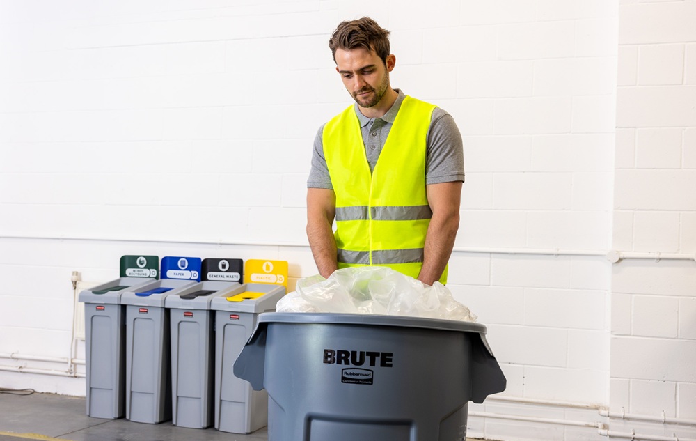 Worker in a high-visibility vest managing waste disposal with labeled recycling bins in the background.