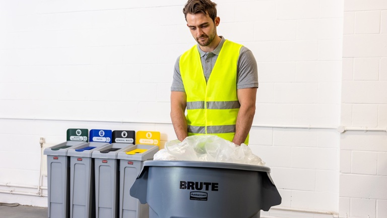 Worker in a high-visibility vest managing waste disposal with labeled recycling bins in the background.